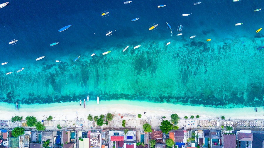 Aerial view of Gili Trawangan featured in this Gili Islands travel guide, showing turquoise water, white-sand beaches and boats anchored along the coastline.