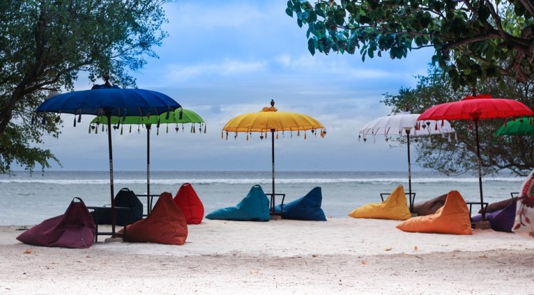 Colorful beach umbrellas and beanbags on Gili Air featured in this Gili Islands travel guide, overlooking the turquoise waters of the Gili Islands. Caption Description