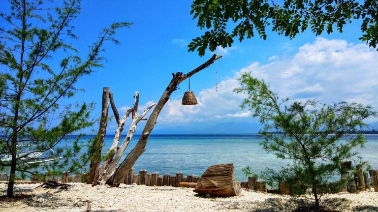 Peaceful tropical beach on Gili Air featured in this Gili Islands travel guide, with crystal-clear water, white coral sand and lush coastal trees.
