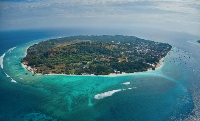 Aerial view of Gili Trawangan featured in this Gili Islands travel guide, showcasing turquoise waters, white-sand beaches and the island's lush tropical landscape.