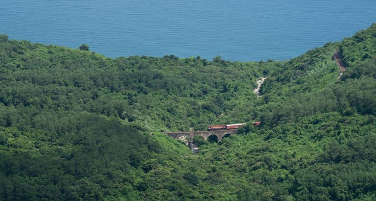 Train crossing the Hai Van Pass through lush green mountains overlooking the South China Sea in central Vietnam Caption Description
