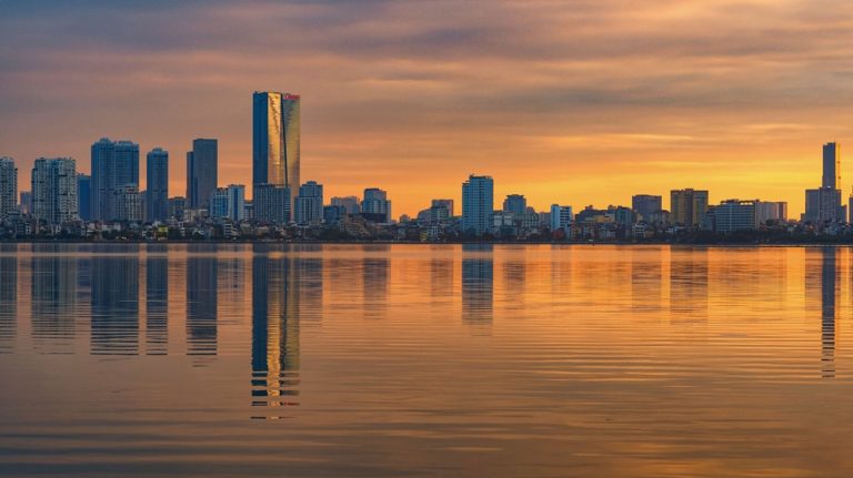 Hanoi skyline reflected in West Lake at sunset with modern skyscrapers and golden evening light in Vietnam