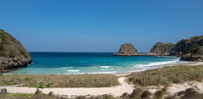 Kuta Lombok Travel Guide: Beautiful white-sand beach with turquoise water and dramatic cliffs near Kuta Lombok, Indonesia.