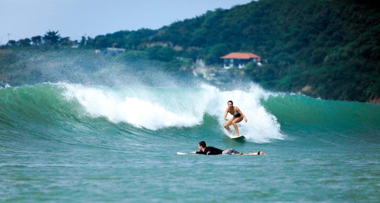 Kuta Lombok Travel Guide: Surfers riding turquoise waves in southern Lombok, one of Indonesia's best destinations for beginner and experienced surfers. Caption Description