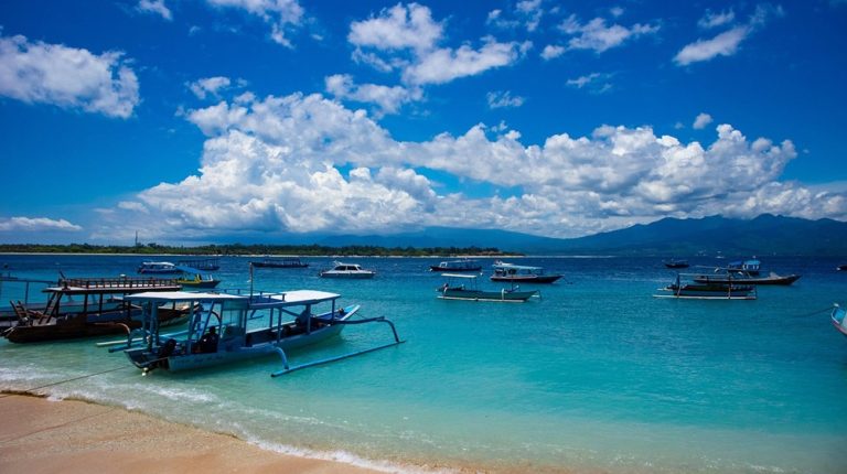 Kuta Lombok Travel Guide: Traditional boats anchored off Tanjung Aan Beach with crystal-clear turquoise water in southern Lombok, Indonesia.