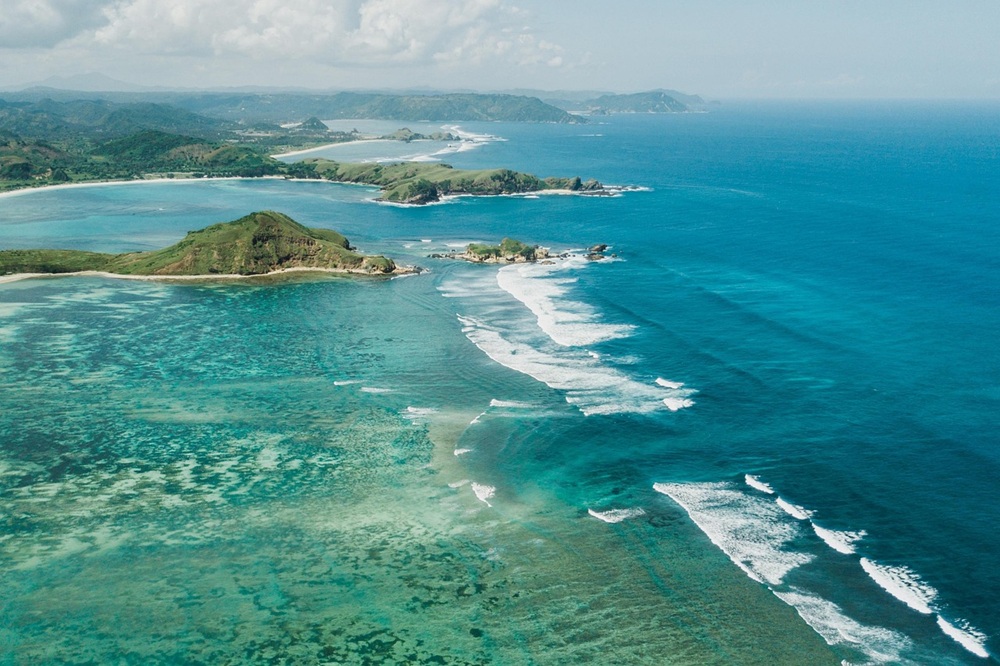 Kuta Lombok Travel Guide: Aerial view of Tanjung Aan Beach with turquoise water, white sand and the southern Lombok coastline.