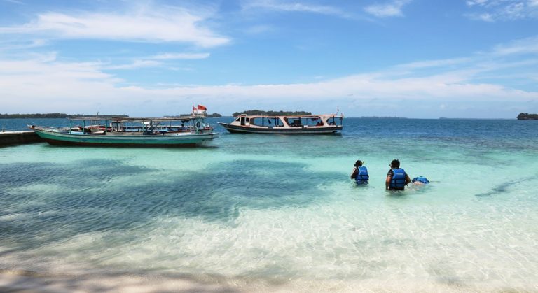 Travelers entering the crystal-clear waters of the Gili Islands on a guided snorkeling tour near traditional boats.