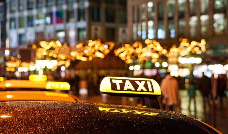 Taxi waiting at night in a busy city, illustrating taxi travel scams around the world and how travelers can avoid common tourist scams. Caption Description