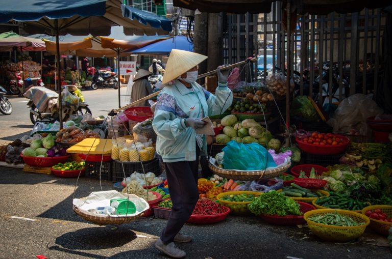 Local vendor carrying fresh produce through a traditional market in central Vietnam