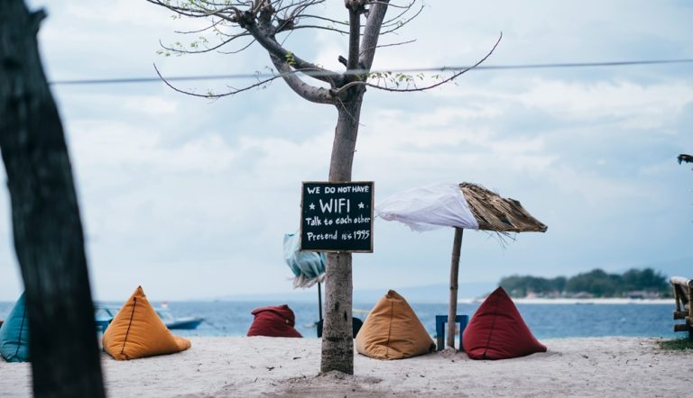 Colorful beanbags on a quiet Gili Islands beach with a sign encouraging visitors to disconnect and enjoy island life.