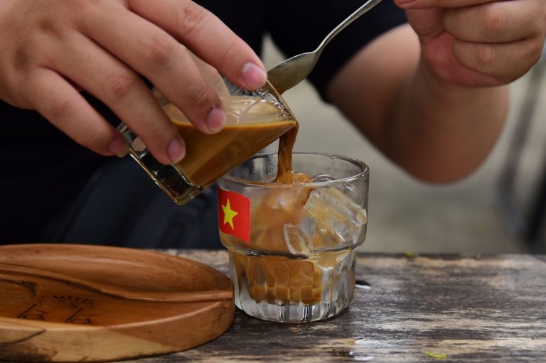 Traditional Vietnamese iced coffee with sweetened condensed milk being poured over ice