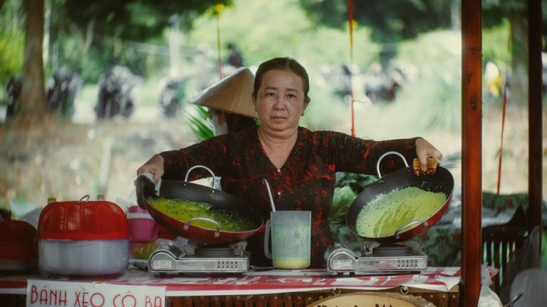 Vietnamese street food vendor cooking traditional bánh xèo pancakes at an outdoor market stall in Vietnam