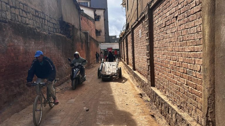 Narrow brick-lined alley in Antananarivo, Madagascar, with a cyclist, motorbike and handcart