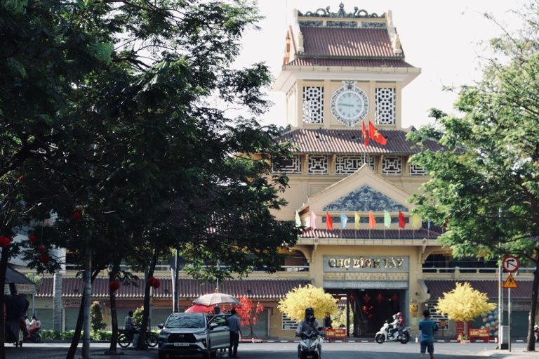 Front entrance of Ben Thanh Market in Ho Chi Minh City surrounded by trees and motorbikes