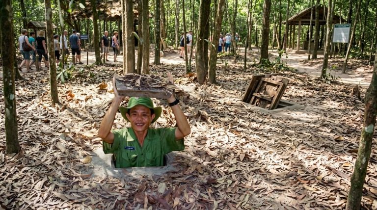 Guide demonstrating a concealed entrance to the Cu Chi Tunnels in the forest near Ho Chi Minh City Caption: Description: