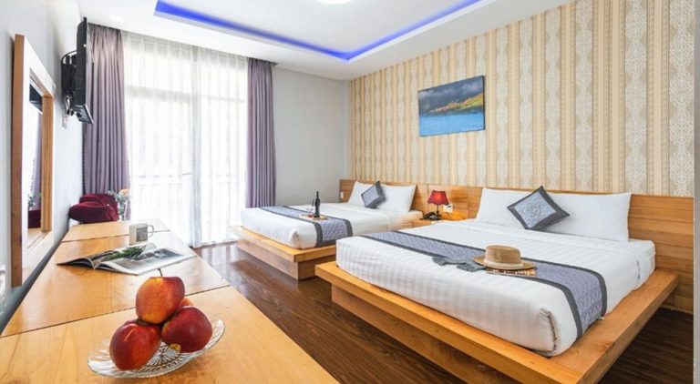 Spacious room at Dalat Wind Hotel in Da Lat with two double beds, wooden furnishings and a private balcony, making it a comfortable choice for families and groups visiting the city. Caption: Description: