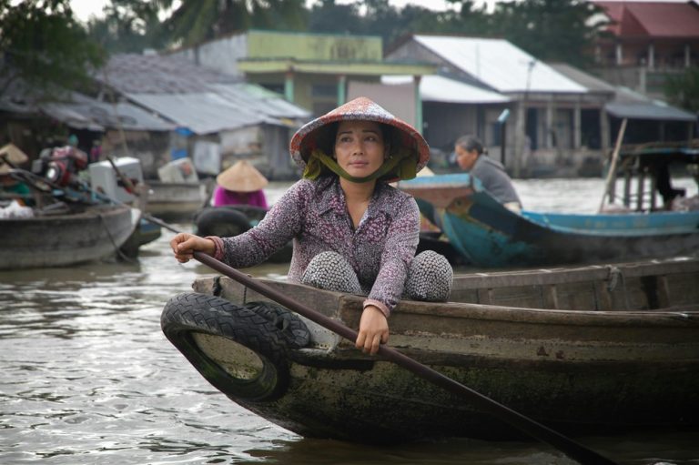 Local vendor paddling a wooden boat through a floating market in the Mekong Delta, showcasing authentic Vietnamese culture and river life.