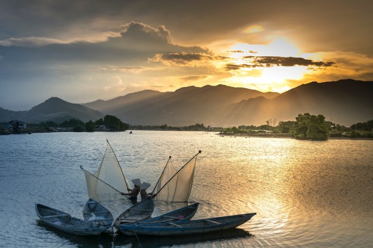 Getting around Vietnam reveals traditional fishermen casting nets at sunset on a peaceful coastal lagoon