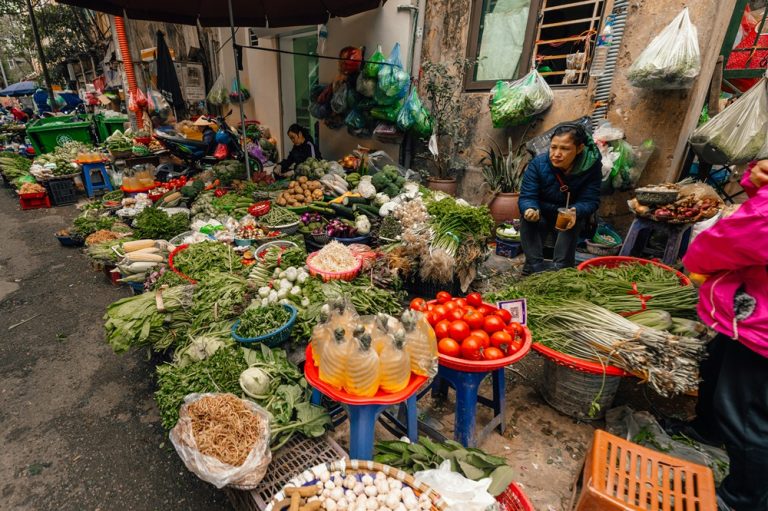Busy Hanoi street market with vendors selling fresh vegetables, herbs and local produce