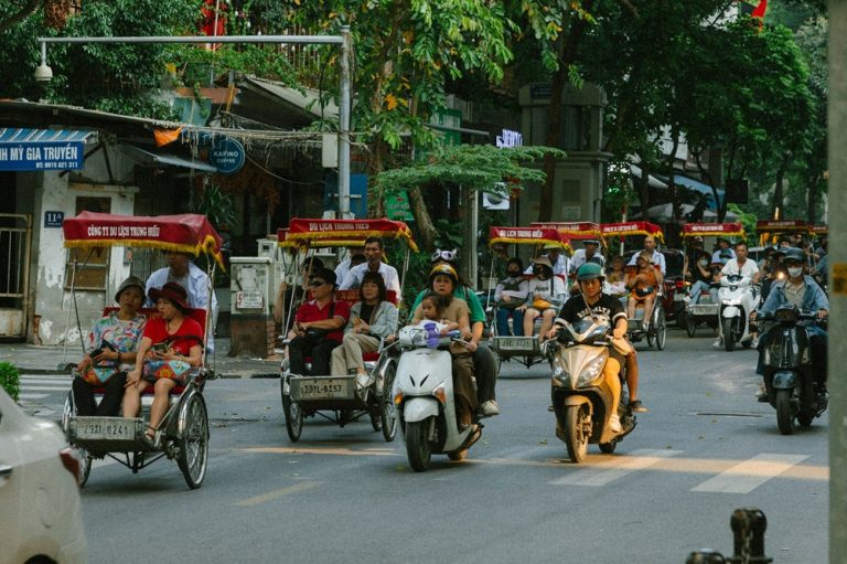 Cyclos and motorbikes moving through a busy street in central Hanoi