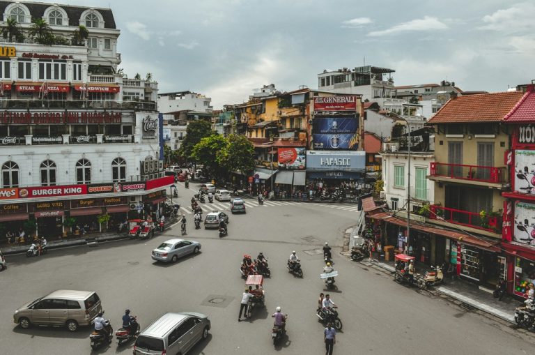 Busy intersection in Hanoi filled with motorbikes, cars and cyclos, highlighting Vietnam travel tips for navigating the country's lively urban traffic.