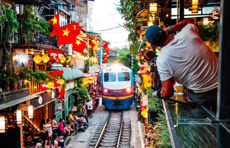 Train passing through Hanoi Train Street lined with cafés and colourful lanterns