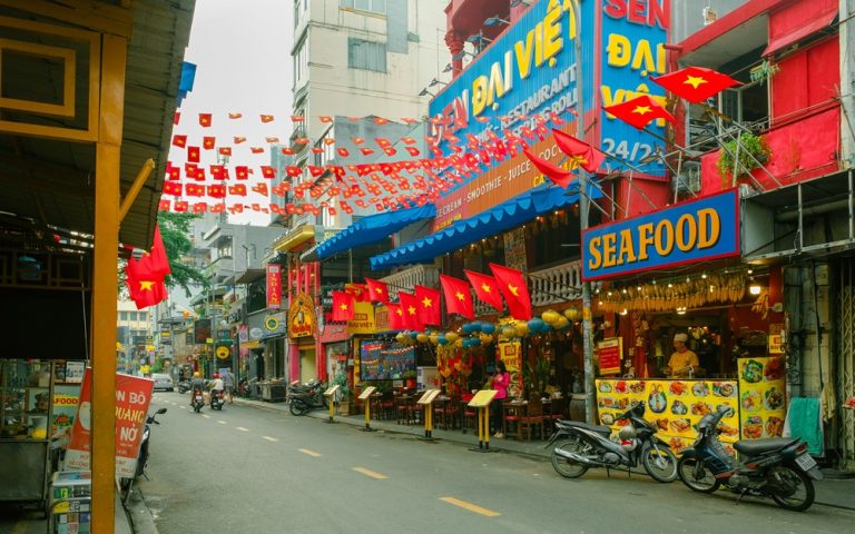 Colourful Ho Chi Minh City street lined with restaurants, motorbikes and Vietnamese flags Caption: Description: