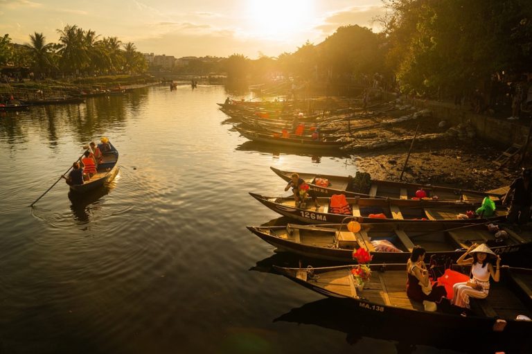 Traditional wooden boats on the Hoai River in Hoi An during golden hour.