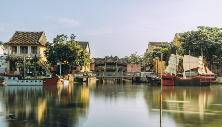 Historic yellow buildings, Japanese Covered Bridge and traditional boats in Hoi An Ancient Town