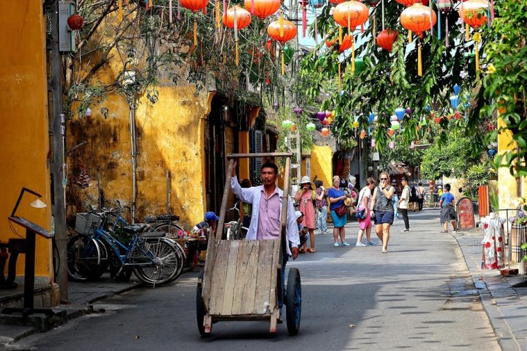 A lantern-lined street with yellow heritage buildings and local life in Hoi An Ancient Town.