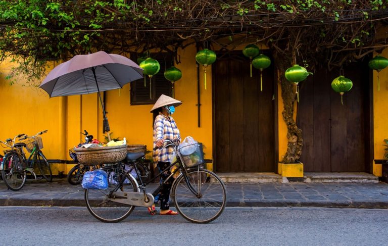 Local woman cycling through Hoi An Ancient Town during the best time to visit Vietnam Caption Description