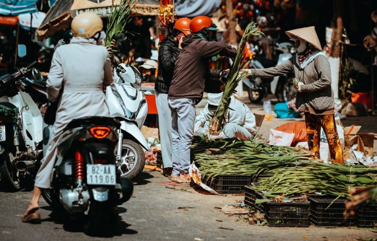 Local street market in Vietnam with vendors selling fresh produce and shoppers on motorbikes