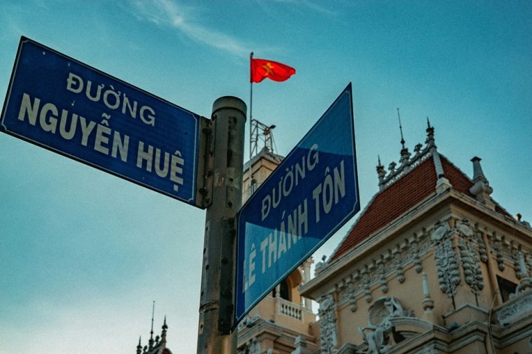 Nguyen Hue street sign in central Ho Chi Minh City with Vietnamese flag and historic architecture Caption: Description: