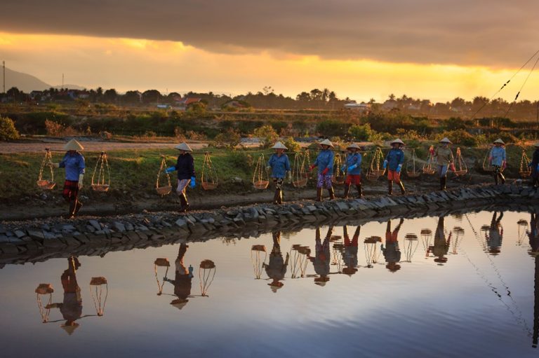 Salt farmers carrying baskets across salt fields at sunset in Vietnam
