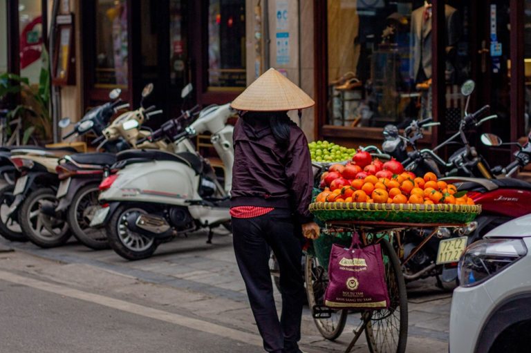 Street vendor pushing a bicycle loaded with fresh fruit along a city street in Vietnam