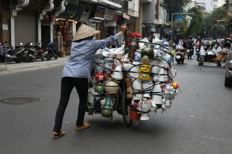 Local street vendor pushing a cart through Hanoi, showcasing authentic Vietnamese street life and traditional commerce.