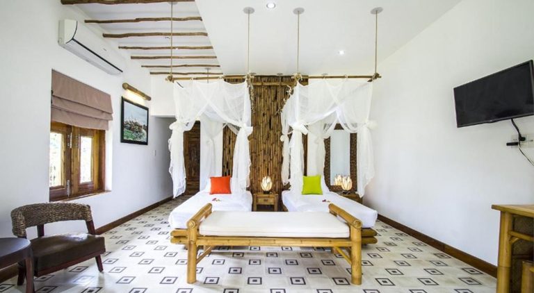 Spacious bamboo-inspired guest room at The Island Lodge in the Mekong Delta featuring twin canopy beds and elegant tropical décor in a peaceful riverside setting.