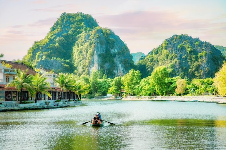 Traditional rowing boat crossing the water beneath limestone karsts at Tam Coc in Ninh Binh Caption: Description: