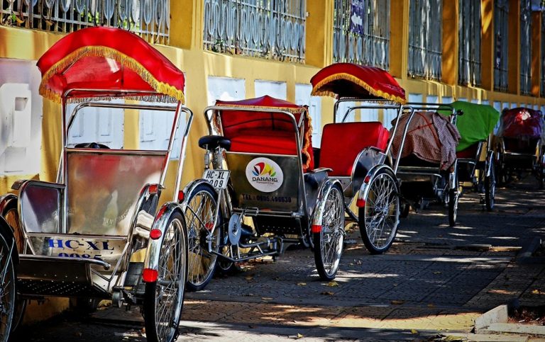 Traditional cyclos with red canopies parked along a street in Da Nang