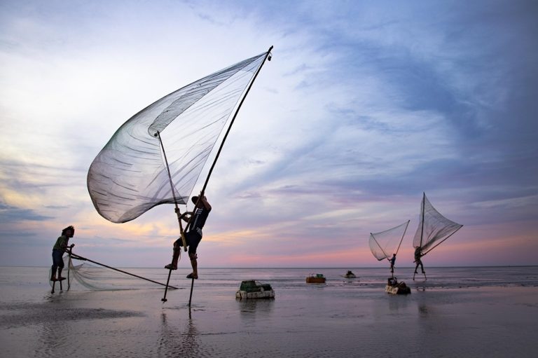 Vietnamese fishermen using traditional fishing nets at sunset along the coast