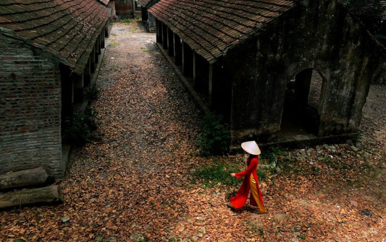 Traditional Vietnamese village with historic buildings and a woman wearing an áo dài, illustrating authentic Vietnam travel tips beyond the country's major cities. Caption Description