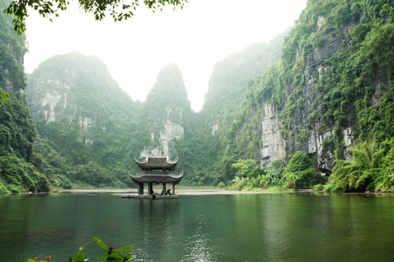 Traditional pavilion surrounded by limestone karsts and emerald waters in Trang An Landscape Complex Vietnam