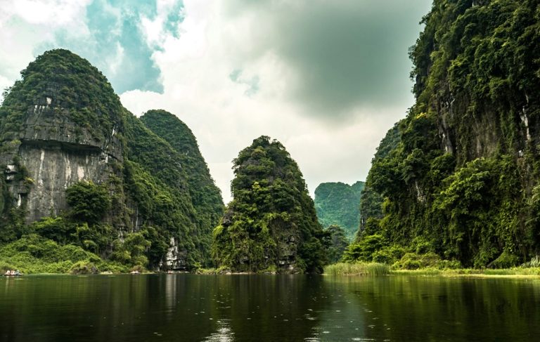 Boat journey through towering limestone karsts and calm waterways at Trang An in Ninh Binh