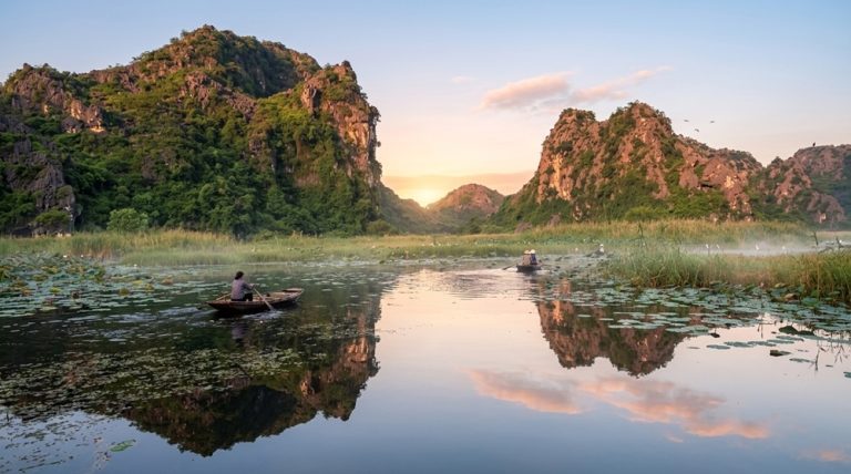 Rowing boats crossing the wetlands beneath limestone karsts at Van Long Nature Reserve in Ninh Binh