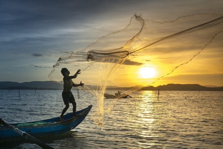 Traditional fisherman casting a net at sunset during the best time to visit Vietnam