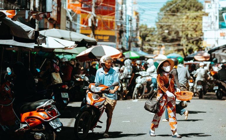 Busy street market in Vietnam with motorbikes, local shoppers and roadside vendors Caption Description