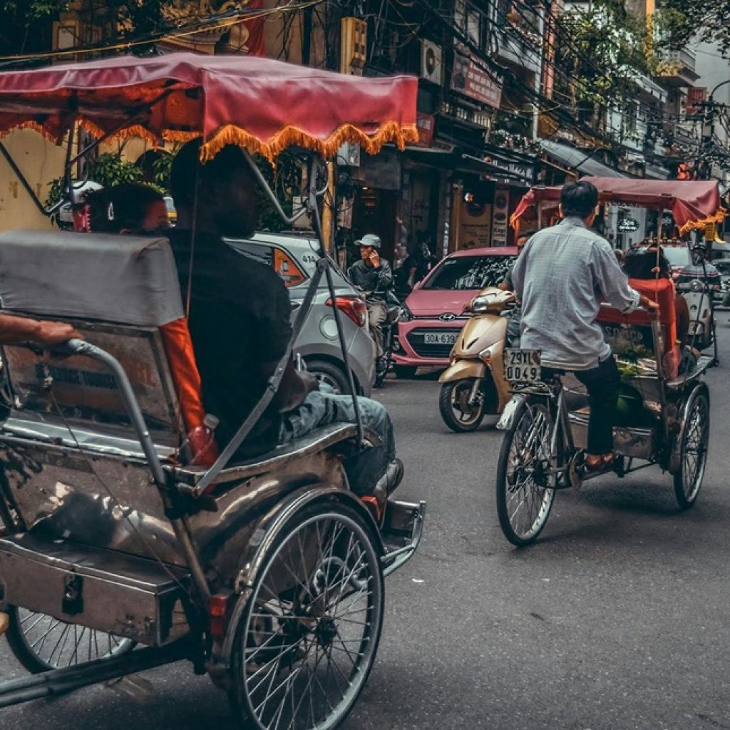 Cyclo riders making their way through Hanoi's busy streets, illustrating practical Vietnam travel tips for first-time visitors exploring the capital.