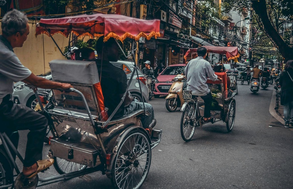 Cyclo riders making their way through Hanoi's busy streets, illustrating practical Vietnam travel tips for first-time visitors exploring the capital.