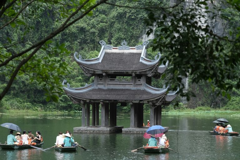Traditional pavilion surrounded by limestone cliffs and rowing boats at Trang An in Ninh Binh