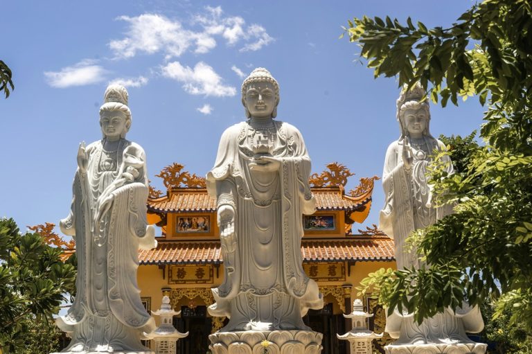 Three large white Buddhist statues standing in front of an ornate temple in Nha Trang, Vietnam